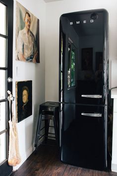 a black refrigerator freezer sitting in a kitchen next to two pictures on the wall