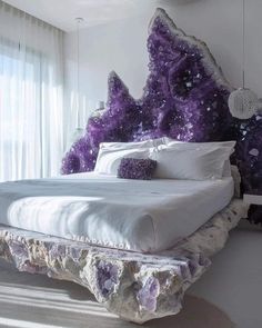 a bed with purple rocks on the headboard and pillows in front of a window