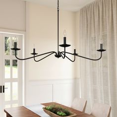 a chandelier hanging over a wooden table in a dining room with white walls