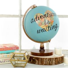 a globe with the words adventure is waiting on it next to some books and candles