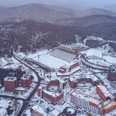 an aerial view of a snow covered campus and surrounding buildings in the distance, surrounded by snowy mountains