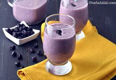 two glasses filled with blueberry smoothie on top of a yellow napkin