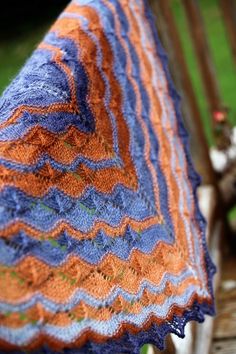 an orange and blue crocheted blanket sitting on top of a wooden bench