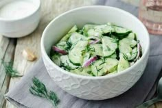 a white bowl filled with cucumbers on top of a table next to spoons