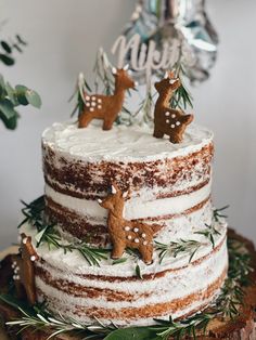 a christmas cake with white frosting and reindeer decorations on top is decorated with greenery