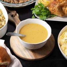 a table topped with bowls of soup and plates of food next to each other on top of a wooden cutting board