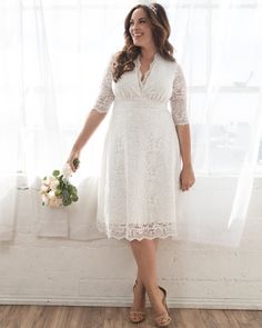 a woman standing in front of a window wearing a white dress and holding a bouquet