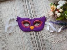 a purple mask sitting on top of a table next to some white flowers and a lace doily