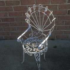 a white metal chair sitting on top of a sidewalk next to a brick wall in front of a building