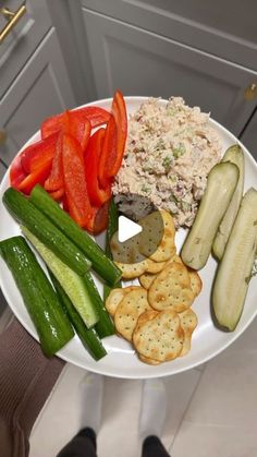 a white plate topped with cucumbers, tomatoes and crackers on top of a counter