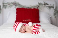 a newborn baby wearing a santa hat and sleeping on a white bed with red pillows