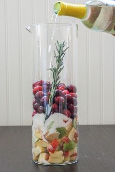 a person pours water into a glass vase filled with fruit and veggies