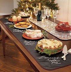 the table is set for christmas dinner with food and wine glasses on it, along with other holiday foods