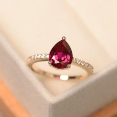 a ring with a red stone and white diamonds on it sitting in a jewelry box