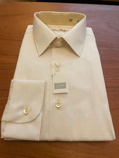 Sophisticated unworn 80s vintage shirt in original packaging in lemon blush polyester cotton mix by Louis Philippe.  Details: straight collar, long sleeves, barrel cuffs, regular fit.  55% Polyester 45% Cotton  Size M Chest 40" Collar 15" Elegant Beige Business Tops, Elegant Beige Business Top, Elegant Beige Tops For Business, Cream Long Sleeve Shirt With Button Cuffs, Elegant Beige Business Shirt, Beige Long Sleeve Top For Business, Classic Beige Business Shirt, Cream Collared Shirt With Button Cuffs, Cream Spread Collar Shirt For Spring