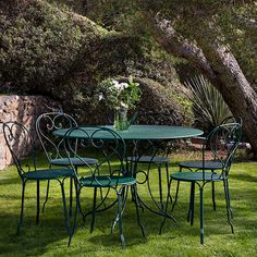 a green table and four chairs sitting on top of a grass covered field next to a tree