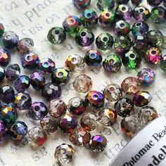 many different colored beads are laying on a table next to a bottle of glue and paper