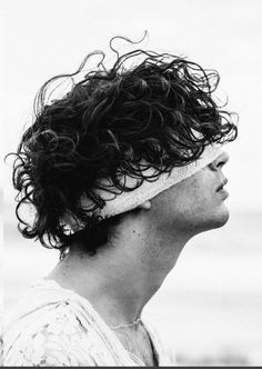 a black and white photo of a man with curly hair wearing a headband on the beach