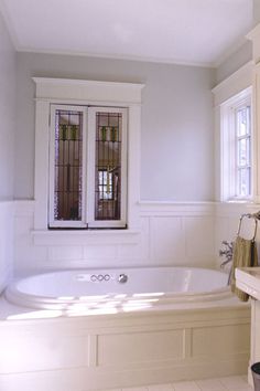 a bath tub sitting next to a window in a room with white walls and floors