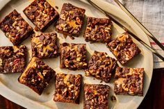 a plate full of brownies with nuts and chocolate toppings on it next to a fork