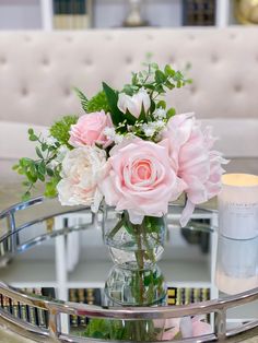 a glass table with flowers on it and candles in the middle, sitting on a couch