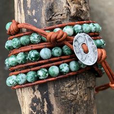 "Triple wrap bracelet featuring polished 6mm round Green Tree Agate beads.  Woven onto a super soft red brown natural leather with coordinating brown nylon thread & and metal button closure. Gemstones vary in color and variation, the bracelet you receive may vary slightly from pictures.  Overall approximate length of wrap is 38 inches, beaded section is 25 inches, with 10 closure options on the 12 inch tail for adjustability. Bracelet width is just shy of one half inch, when wrapped around wrist and stacked three times the wrap is approximately 1.25\" in width. This wrap goes around my 6.5\" wrist about three and a half times.  This wrap bracelet is intended to go around your wrist three times.  It will wind a bit longer on a smaller wrist & on a larger wrist it could be a bit less than a Affordable Green Bohemian Wrap Bracelet, Triple Wrap Bracelet, Tree Agate, Green Trees, Metal Buttons, Agate Beads, Thing 1 Thing 2, Natural Leather, Wrap Bracelet