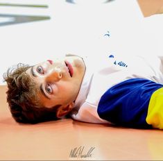 a young man laying on the floor with his head down and eyes open, looking up