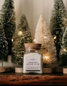 a jar filled with frosted sugar next to small trees and lights on a mantle