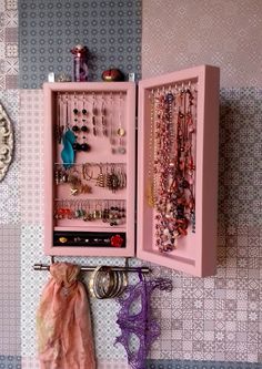 a pink cabinet with jewelry hanging from it's sides and a scarf on the wall