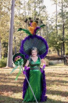 a woman in a green and purple dress holding a pole with feathers on it's head