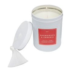 snowdrops and freesia candle in a white tin with a tasseled lid