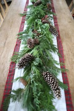 a long table with pine cones and greenery on it, along with plaid runner