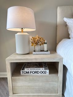 a nightstand with a lamp on top of it next to a book and a bed