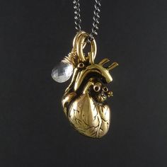 My Anatomical Heart necklace, beautifully detailed, cast in solid bronze and plated in 24 karat gold. A crystal clear quartz, beautifully faceted and skillfully wrapped in sterling silver gold filled wire. Sometimes I really wish I was a better photographer, to do this beauty the justice it deserves. The heart itself is as anatomically correct a heart as you'll find, lovingly detailed, meticulously crafted. Every artery and valve, every atrium and ventricle are captured in this pendant, and it h Brass Heart Pendant Jewelry For Anniversary, Brass Heart Charm Jewelry For Gift, Handmade Brass Heart Pendant Jewelry, Unique Heart-shaped Gold Jewelry, Unique Gold Heart-shaped Jewelry, Brass Heart Pendant Jewelry With Charms, Brass Heart Pendant Charms Jewelry, Unique Gold Heart Pendant Jewelry, Unique Gold Jewelry With Heart Charm