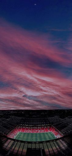 an empty soccer stadium with red and white clouds in the sky at dusk or dawn