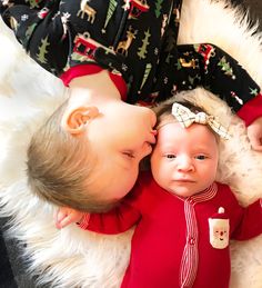 two babies laying next to each other on top of a white fur covered floor with black and red pajamas