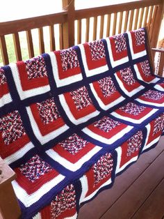 a red, white and blue crocheted blanket on a wooden porch with a bench