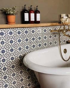 a bath tub sitting next to a shelf with bottles on it and soap dispensers