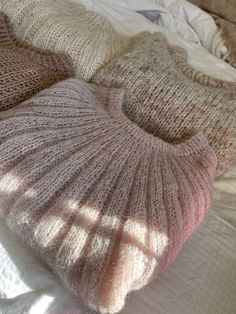 three knitted sweaters laying on top of a bed next to pillows and blankets