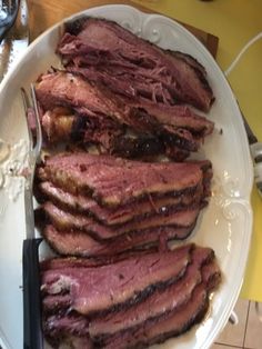 a white plate topped with sliced up meat next to a knife and fork on top of a table