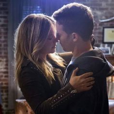 a man and woman embracing each other in front of a brick wall with lights on it