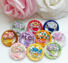 nine different colored hair clips with flowers on them and a pink rose in the background