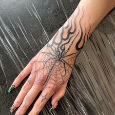 a woman's hand with a spider web tattoo on her left arm and green nail polish