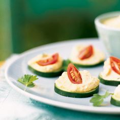 cucumbers with tomatoes and cream cheese are on a plate next to a cup