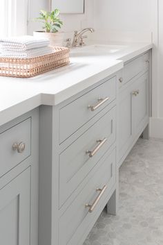 a bathroom with white counter tops and gray cabinetry, along with a basket full of towels