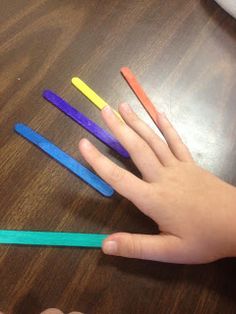 a child's hand holding four colored toothbrushes on top of a wooden table