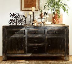 an old wooden dresser with candles and other items on it's top, in front of a white wall