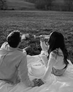 a man and woman sitting on a blanket with a cake in front of them,