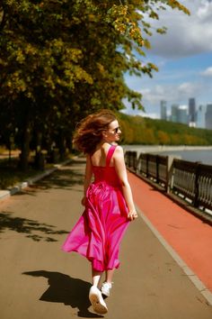 a woman in a pink dress is walking down the street with her hair blowing in the wind