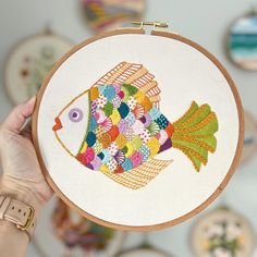 a person holding up a colorful fish embroidery on a hoop